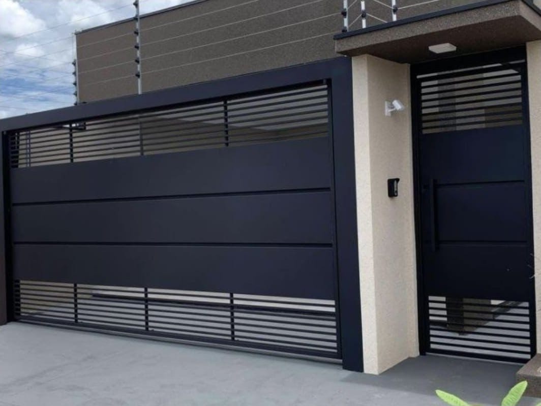 Portão basculante de aço com portão social ao lado, instalado na garagem de uma residência