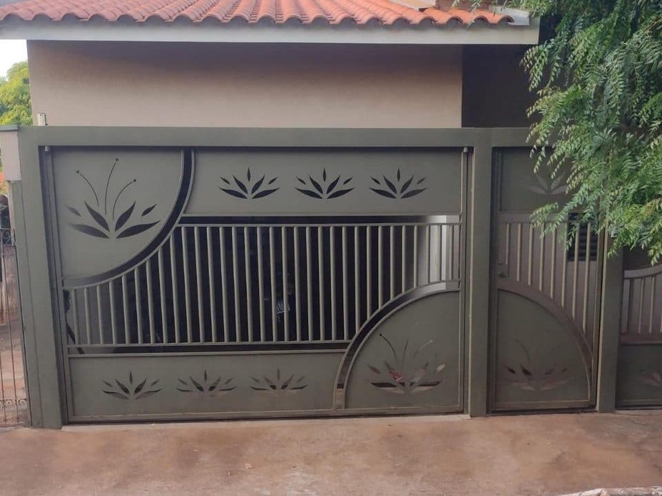 Portão de aço com grade vertical e recortes decorativos de folhas, com portão social, instalado na frente de uma casa